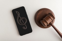 Smartphone with treble clef sign on display and judges hammer. Illegal use of music concept. Digital piracy