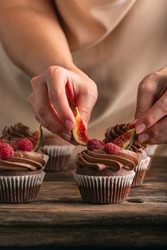 Pastry chef decorates muffin with raspberries and figs. Close up photo of cupcakes preparation. Vertical frame.