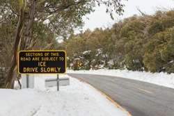 Winter road in Australian alps ice on road yellow lane marking Drive Slowly warning sign