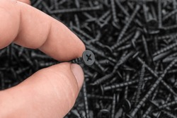 Hand holding self-tapping screw over background of black self-tapping screws. Close up.