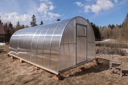 Polycarbonate greenhouse in the garden. The greenhouse is used for growing organic plants at home. Growing vegetables and fruits, gardening. The light is the setting bright sun.