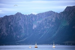 Mountain ridges of nordic fjords colored in blue with three vessels in the foreground, Lofoten Islands, Sortland, Norway