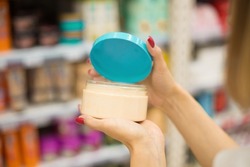 A woman in a cosmetics store holds a jar of body cream or hair mask in her hands. A client buys a shampoo or balm or hair mask from a cosmetics store. The choice of cosmetics in a beauty salon