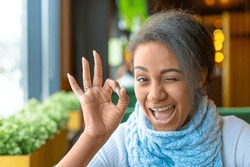Portrait of an African American woman with a video call. She showing allright gesture. Close-up picture.