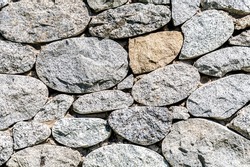 Rough stone wall as creative background texture. Natural stones masonry with uneven seams. Stone wall background