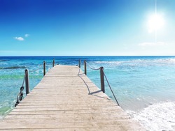 Pier or wooden bridge on a tropical beach with clear sky, sun and turquoise water. sea scene or beach background, summer holidays. Summer background with copy space.