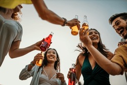 	
Low angle view of a group of people with their cocktail bottles in a toast, clinking them together and expressing their excitement for the upcoming celebration.
