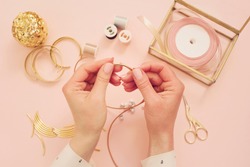 Jewelry designer workplace. Woman hands making handmade jewelry. Freelance fashion femininity workspace in flat lay style. Pastel pink and gold