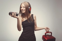 Joyable attractive fashion pretty girl listening music with headphones, speaker, record player, holding them in hands and wearing red gloves, take pleasure with song. Lifestyle woman concept