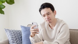 Asian man looking at smartphone in living room