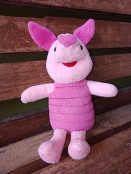 cute little pink piglet doll sitting on a wooden chair.