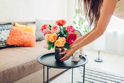 Woman puts vase with flowers roses on table. Housewife taking care of coziness in apartment. Interior design and decor