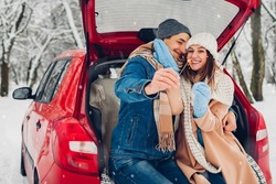 Young couple in love burning sparklers in car trunk in snowy winter forest. People relaxing outdoors during Christmas season road trip