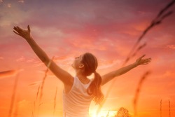 Free and happy woman raises arms against the sunset sky