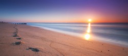 Footsteps in the sand during a sunrise panorama