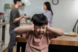 Young little Asian kid feel sad upset, boring while parent fighting arguing or quarrel, sad little boy frustrated with psychological problem caused by mom and dad family conflicts or violence concept.
