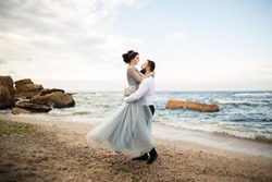 Wedding. Wedding by the sea. Young couple in love, bearded groom and bride in wedding dress at the seaside. Couple in love walking around the sea and the rocks near the place of the wedding ceremony.