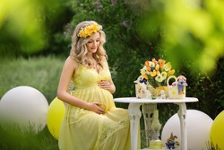Young and beautiful pregnant woman in yellow dress holding belly in spring or summer garden
