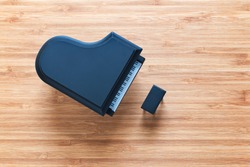 Black toy grand piano on a wooden floor with stool standing near it. Top view. Music concept.