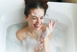 Happy woman bathes in a bathtub white foam on her face fun emotions