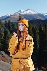 A young woman smokes an e-cigarette in the mountains while hiking