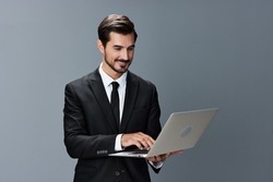 Man business stares at laptop and works thoughtfully online smiling over the internet in business suit video call business talks on gray background copy place