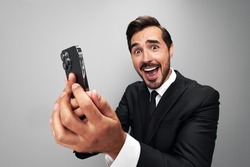 Man businessman holding phone in hand looking into screen video call and selfies and smile with teeth. Close-up wide angle photo gray isolated background