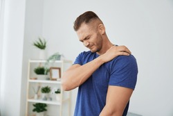 Man back neck and shoulder pain, inflammation of muscles and ligaments rupture during sports, inflammation and injury, in a blue t-shirt at home