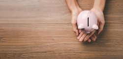 Woman hand holding piggy bank on wooden background, saving, charity, family finance plan concept, fundrasing community care, superannuation, financial crisis concept