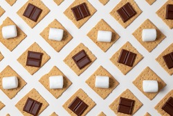 s'mores ingredients. graham cracker squares with chocolate bars, marshmallows on a white background. 