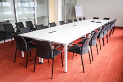 Empty, clean and bright meeting room with red carpet, flipchart, long table and black chairs. Suitable for meetings, seminars, teaching and lectures. Representative space for business. 