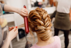 Woman hairdresser making hairstyle to blonde girl in beauty salon.