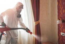 Pest control specialist in white hazmat contractor working in flat and hotel.