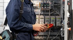 Electrician engineer checks electrical circuit in control panel for high current and voltage, starting and commissioning relays for industrial production.