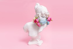 Sculpture of antique girl made of plaster in medical mask with flowers against coronavirus pandemic and common cold. Beauty salon fashion in pink background concept.