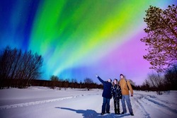 Company friends tourist looks aurora northern lights night at forest, soft focus.