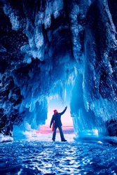 Adventure travel winter Lake Baikal tourist man with red scarf background ice grotto and cave, frozen icicles.