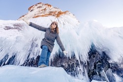 Happy young woman tourist in sunglasses on background ice cave grotto, frozen waterfall or lake Baikal.