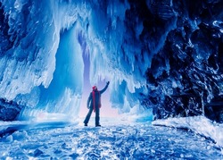 Beautiful adventure Travel winter landscape with people. Tourist man in Ice blue cave or grotto on frozen lake Baikal.