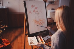Artist, a European girl, paints painting on canvas with watercolor in her workshop and art school.