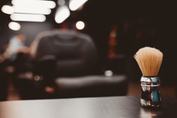 Barbershop. Brush for shaving beard along with bowl, blurred background of hair salon for men, barber shop