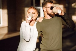Young couple having fun talking, drinking coffee and using the phone while walking in the morning city. Relaxation, youth, love, lifestyle, selfie, blogging.