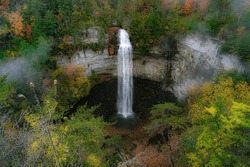 Photo of Falls Creek Falls in an autumn morning mist. Fall colors surround a ribbon of water falling from a rock cliff into a dark pool below. Taken at Falls Creek Falls State Park in Tennessee.  