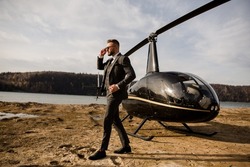 Rich man talking on the phone with business partners. Helicopter stands on the beach