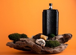 Black perfume bottle with water drops on  stand made of wood and moss. Natural perfumes, woody scents in men's perfume.