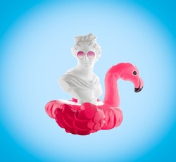 Collage of female head statuette with  inflatable flamingo and  pink glasses on  blue background. Summer travel poster concept.
