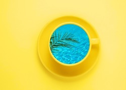Creative summer minimal art poster. Yellow coffee cup with blue water and palm leaf on yellow background. Art collage. Top view.