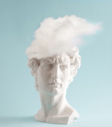 White plaster statue head of David with cloud  on pastel blue background. Minimal art poster.