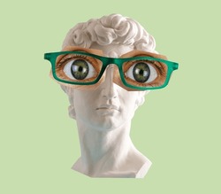 White plaster statue head of David  with big eyes and glasses green background. 