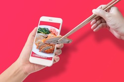 hand using chopsticks to clamp the roasted duck from application to made order food online via mobile smartphone, isolated on red background. online food order and delivery service advertise concept.
